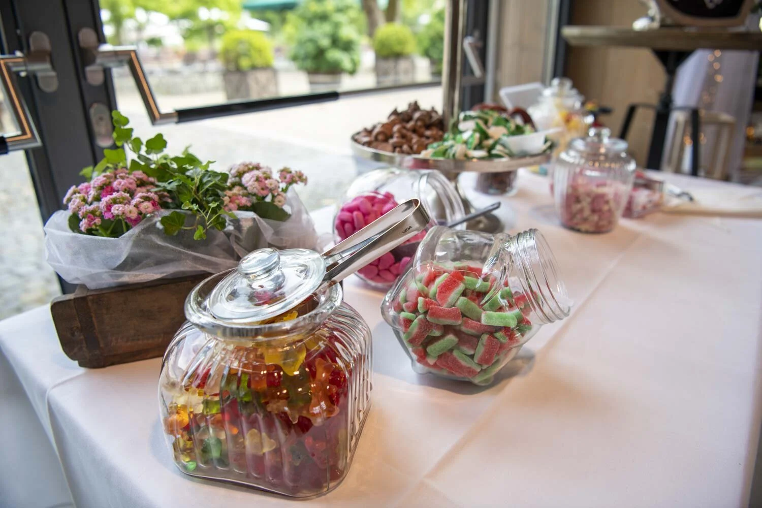 Große Gläser mit Fruchtgummi und Süßigkeiten auf einem weiß gedeckten Tisch