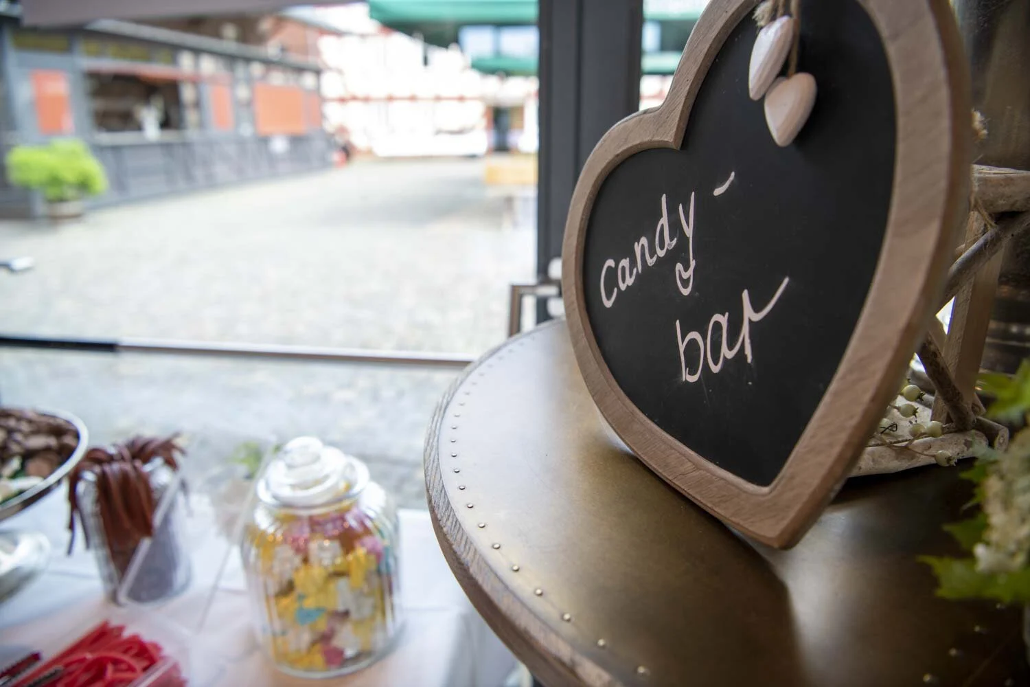 Herzförmiges Tafelschild mit der Aufschrift Candy-Bar neben Süßigkeitengläsern