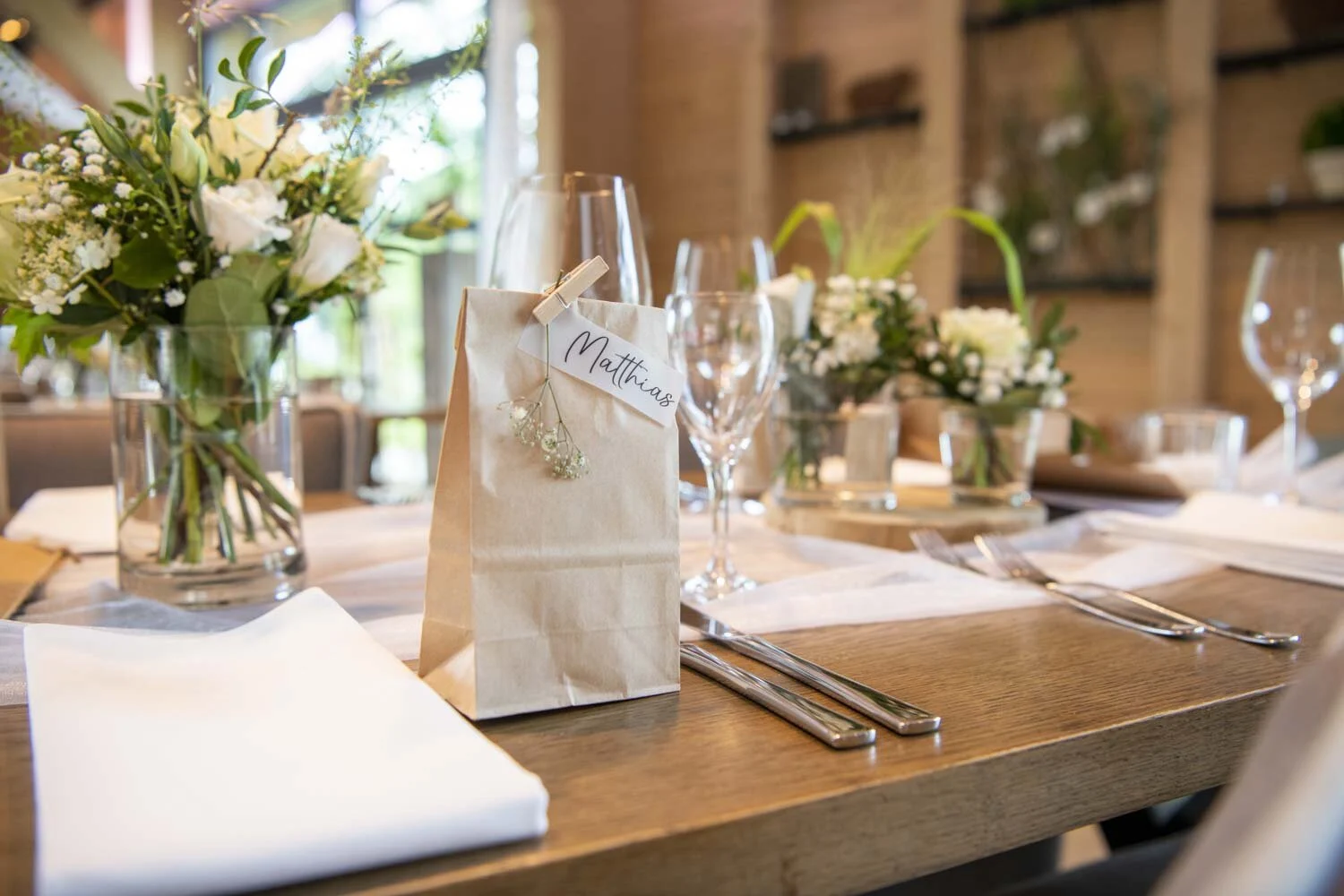 Gedeckter Tisch mit Blumen, Gläsern und einem Papiertütchen als Platzkarte