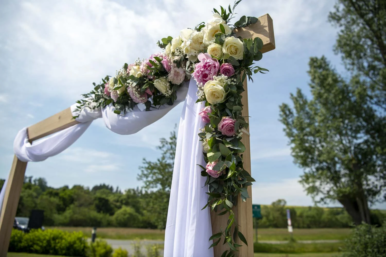 Traubogen aus Holz mit Rosen, grünen Ranken und weißem Tuch vor blauem Himmel