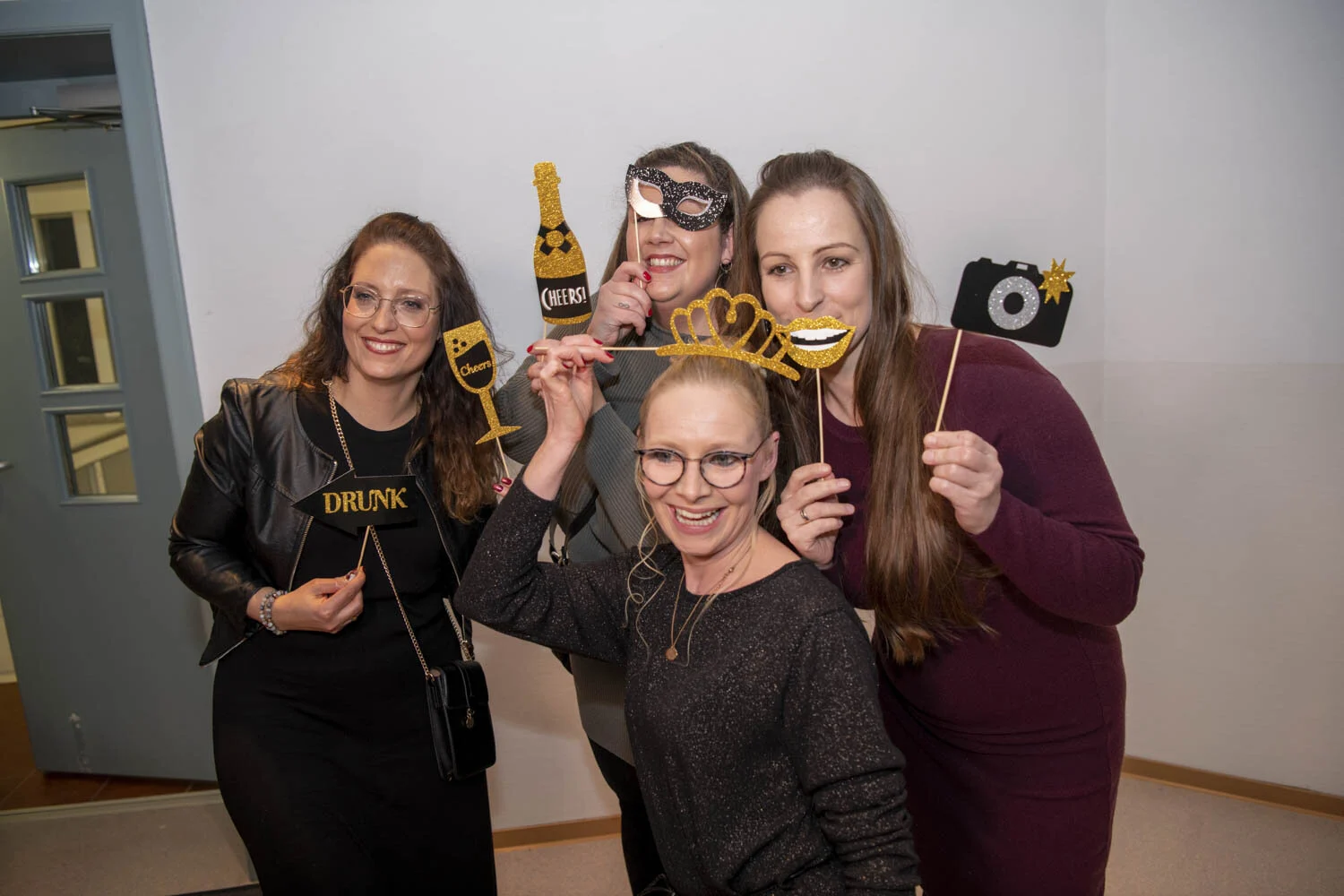Vier Frauen posieren mit Brillen, Kronen und Schildern an der Fotobox