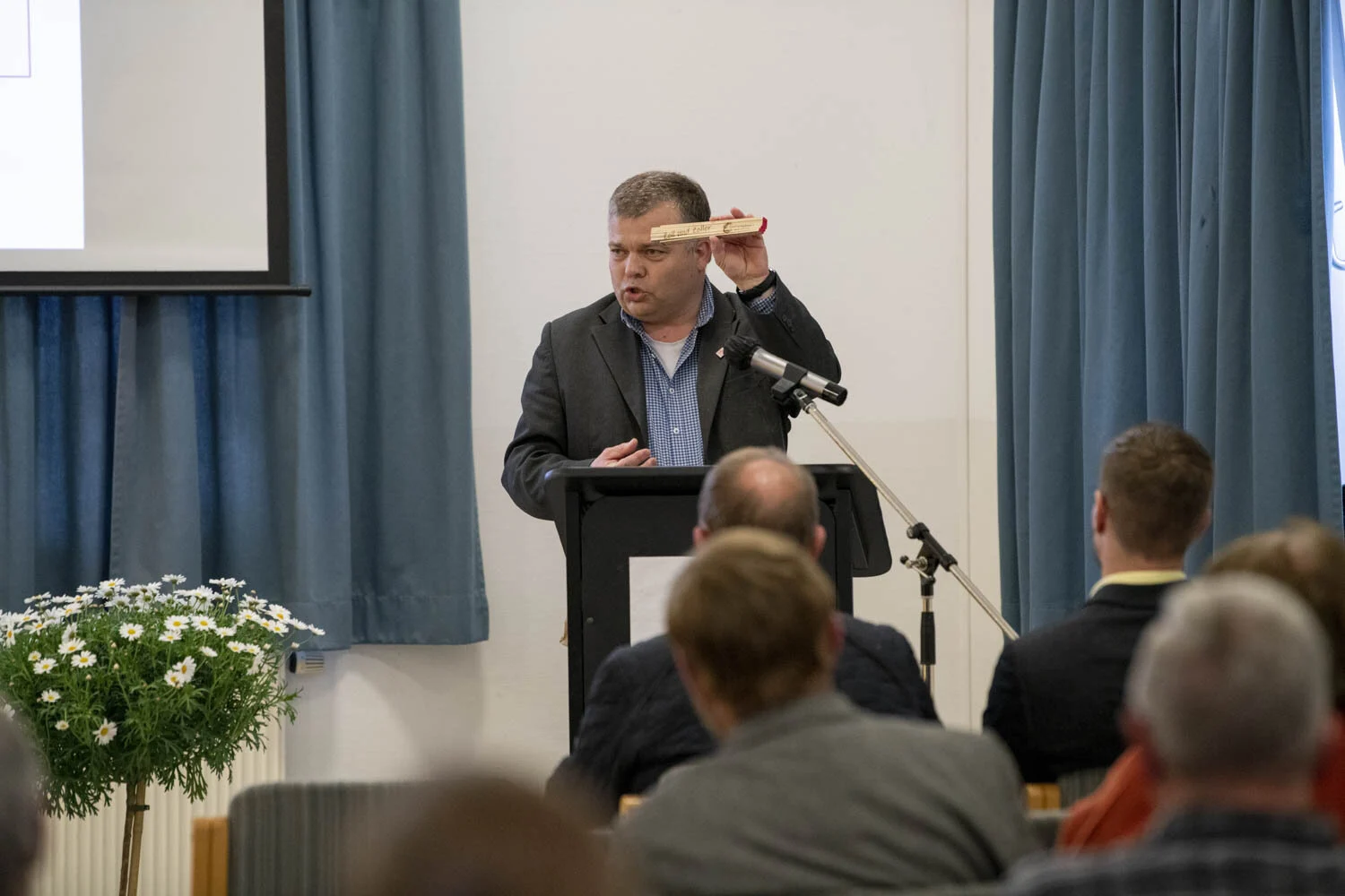 Redner am Pult hält einen Zollstock in die Höhe