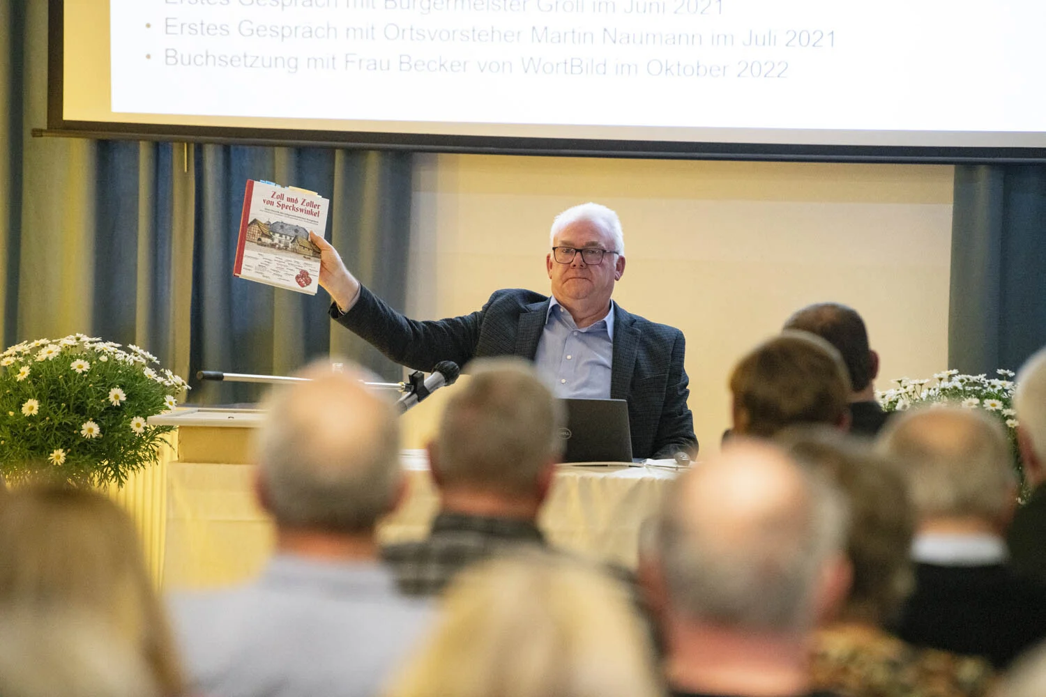 Autor hält am Tisch sein Buch Zoll und Zoller von Speckswinkel in die Höhe