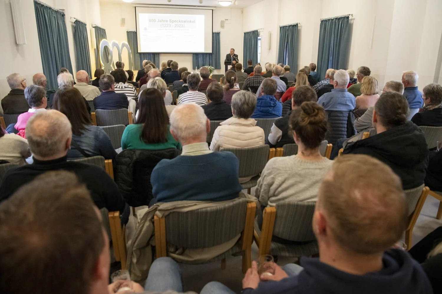 Zuhörerinnen und Zuhörer sitzen im voll besetzten Saal vor der Leinwand
