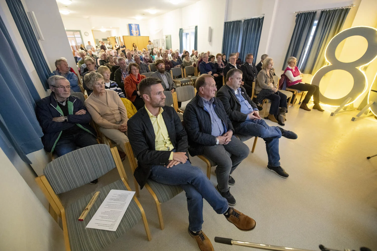 Gäste in der ersten Reihe neben einer leuchtenden Acht