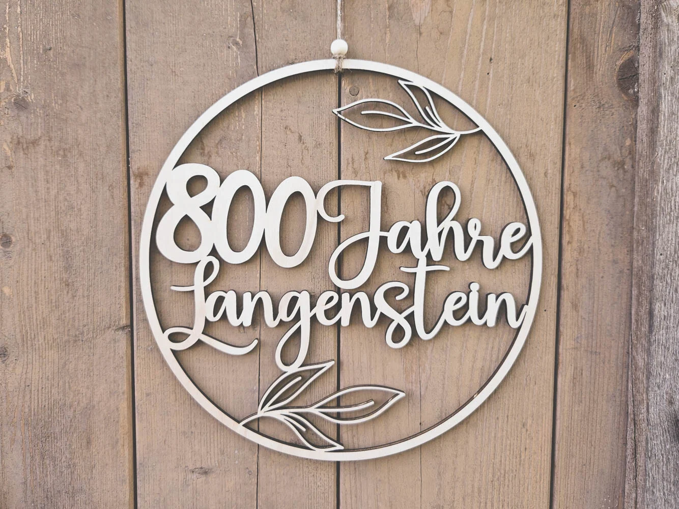 Runder Holzreifen mit dem Schriftzug 800 Jahre Langenstein und zwei Blattzweigen