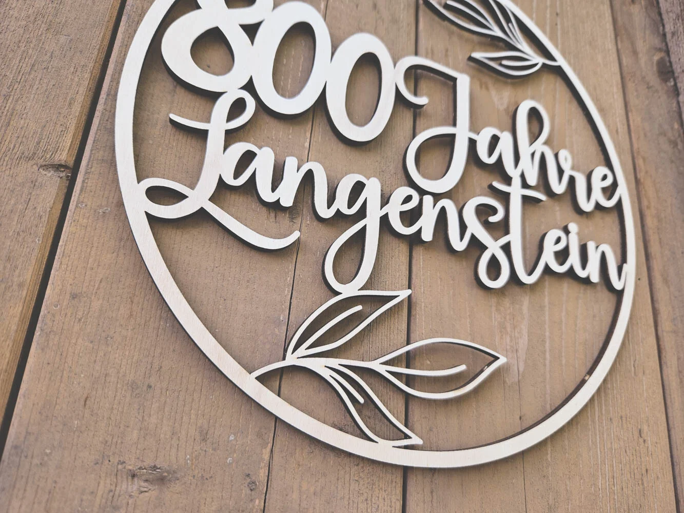 Nahaufnahme der geschwungenen Schrift und der filigranen Blätter auf hellem Holz