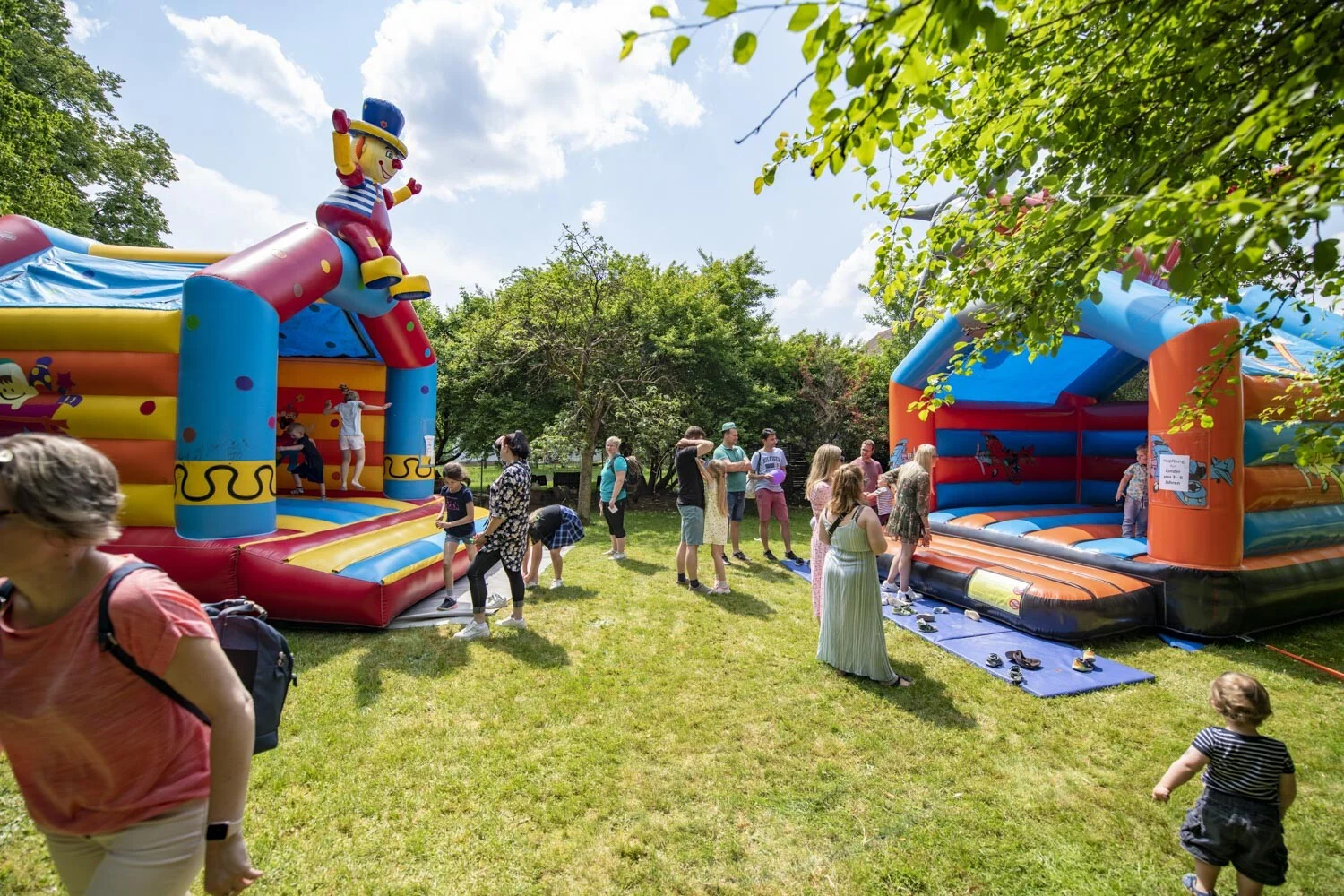 Zwei bunte Hüpfburgen auf einer Wiese, davor spielende Kinder