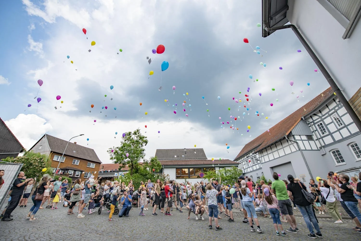 Bunte Luftballons steigen über einer Menschenmenge zwischen Fachwerkhäusern auf