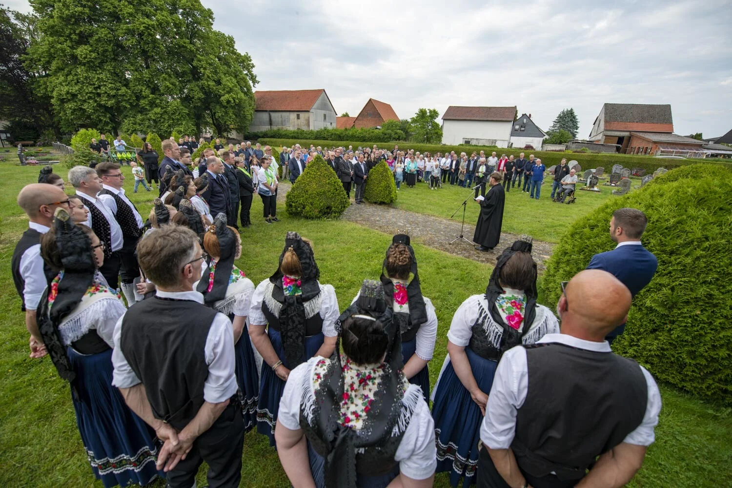 Trachtengruppe steht auf einer Wiese und hört einer Rede zu