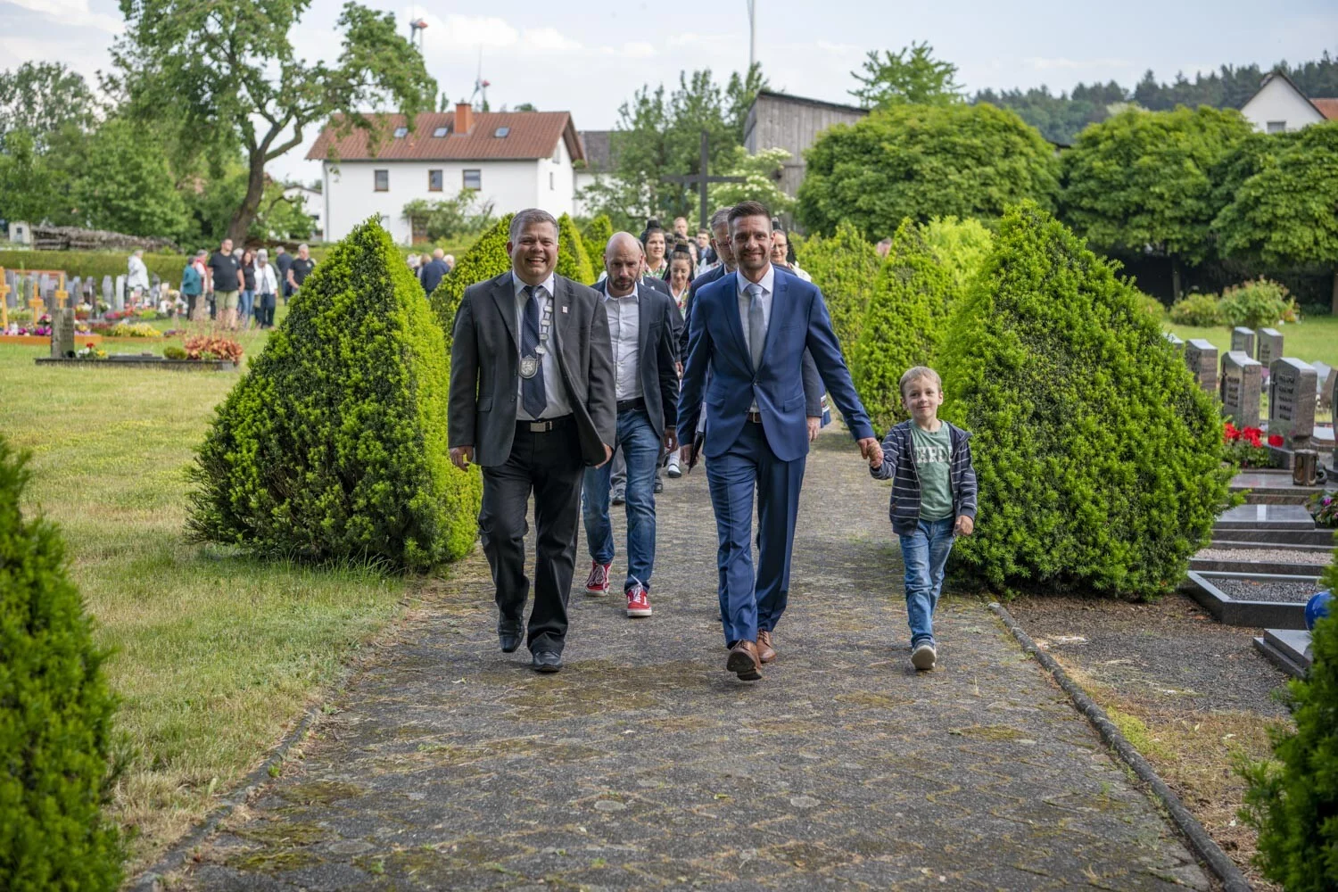 Ehrengäste in Anzügen gehen mit einem Jungen einen Weg entlang