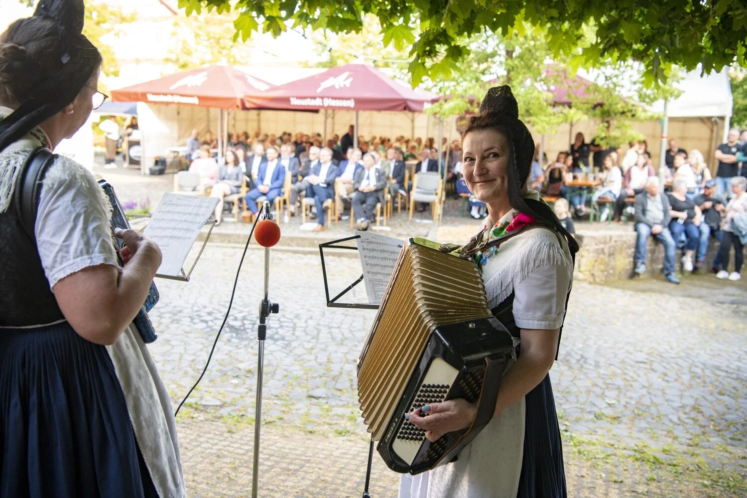 Musikerin in Tracht spielt Akkordeon, im Hintergrund sitzende Gäste