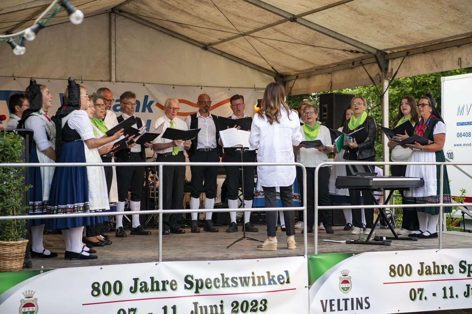 Chor mit Notenmappen singt auf der Bühne unter dem Zelt