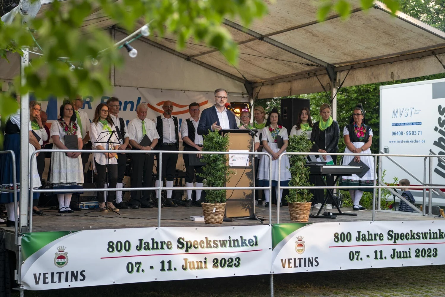 Redner am Pult auf der Bühne, dahinter Chor und Trachtengruppe