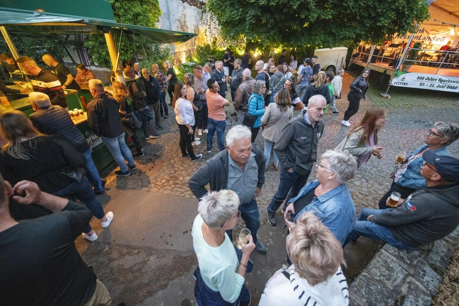 Gäste stehen am Abend zwischen Ständen auf dem Festplatz