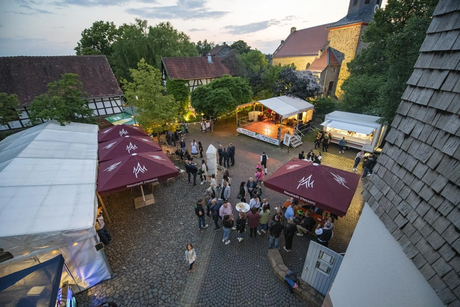 Festkommers am Abend: Festplatz mit Zelten und Gästen zwischen Fachwerkhäusern von oben