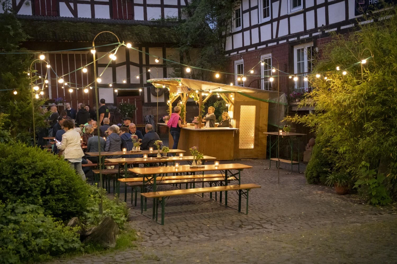 Bierbänke und eine kleine Holzbar unter Lichterketten vor Fachwerkhäusern