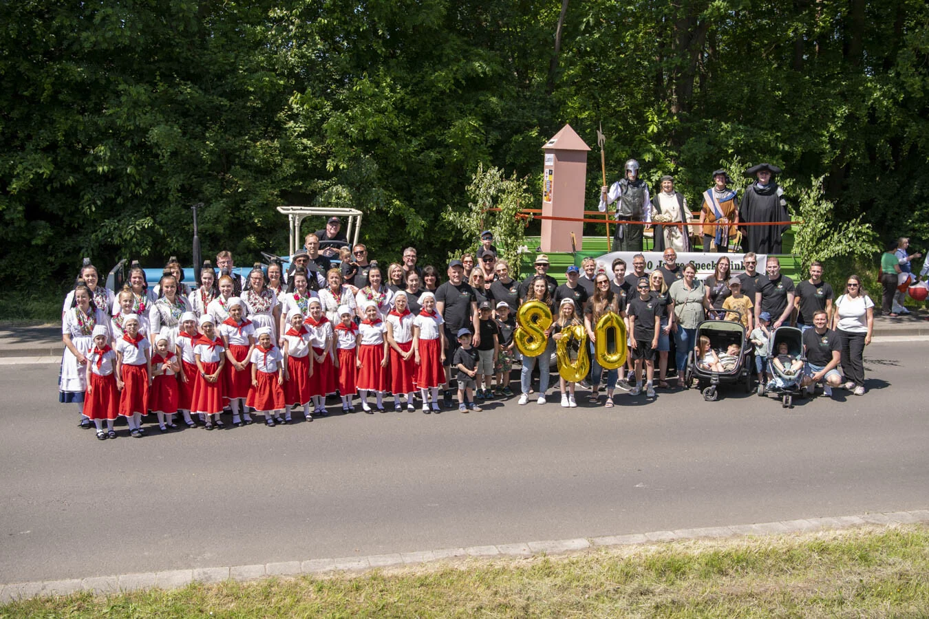 Gruppenbild der Speckswinkler Teilnehmenden in Tracht und Shirts vor dem Festwagen