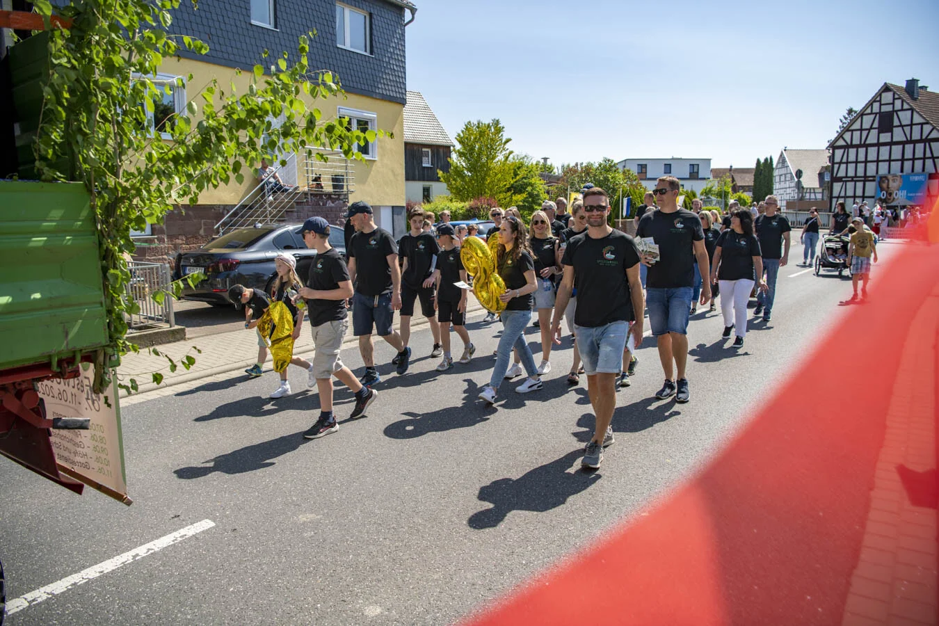 Gruppe in schwarzen Shirts folgt dem Festwagen eine Straße entlang