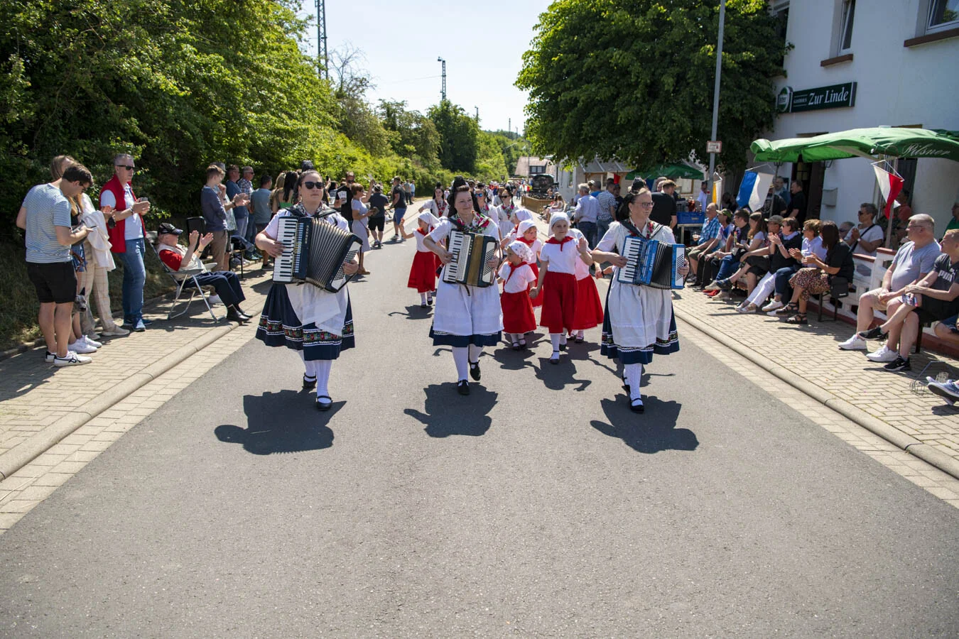 Trachtengruppe mit Akkordeons zieht die Straße entlang, am Rand Zuschauer