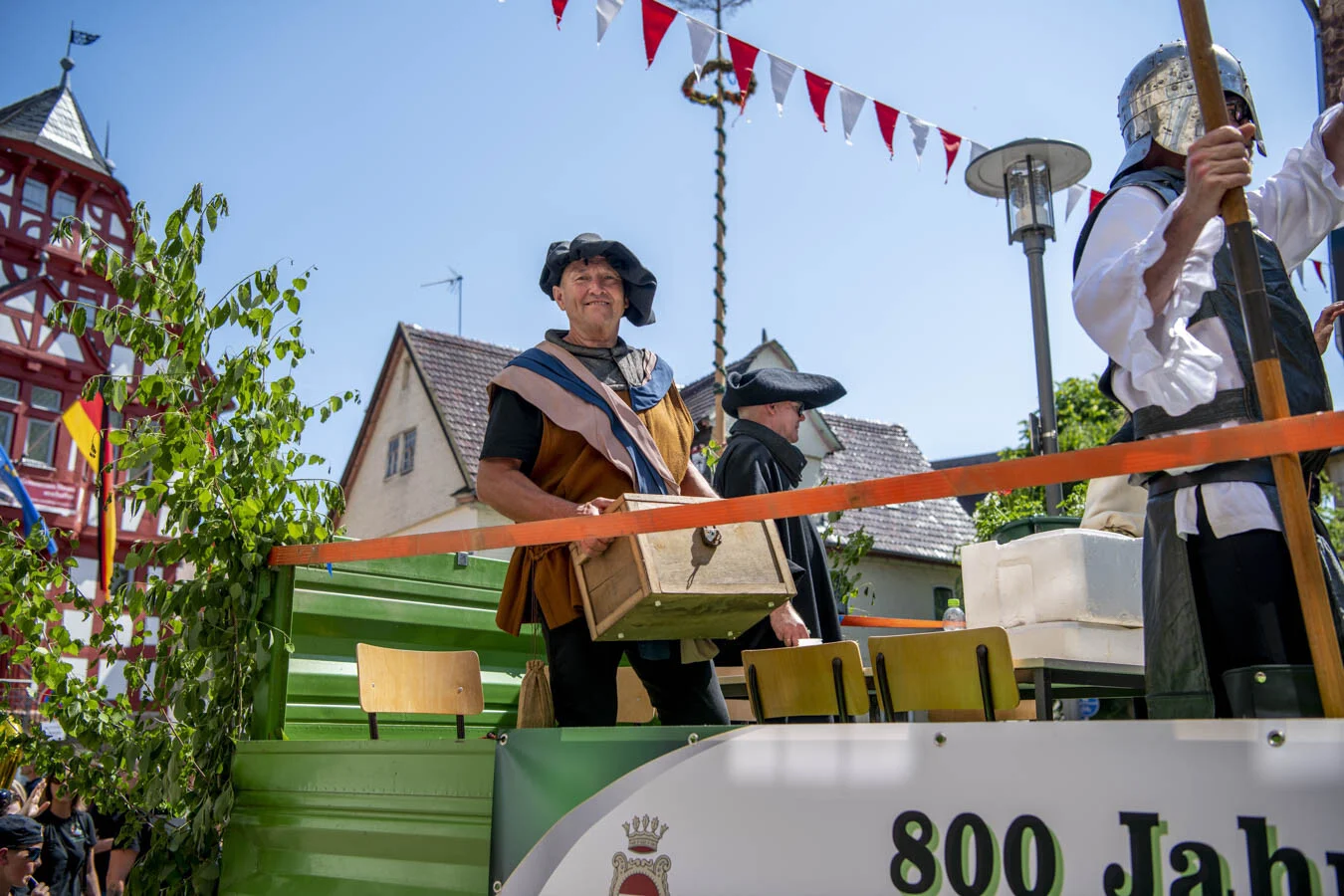Darsteller mit Hut und Kiste auf dem Festwagen, darüber Wimpelketten