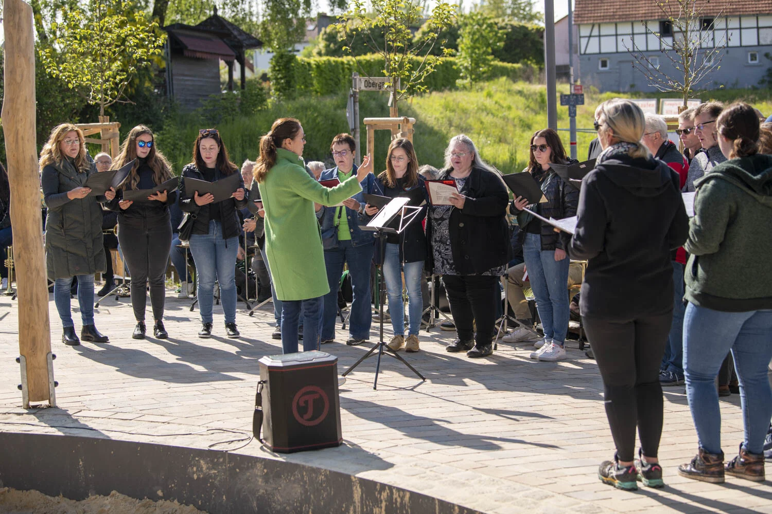 Chor singt mit Notenmappen unter der Leitung einer Dirigentin im Freien