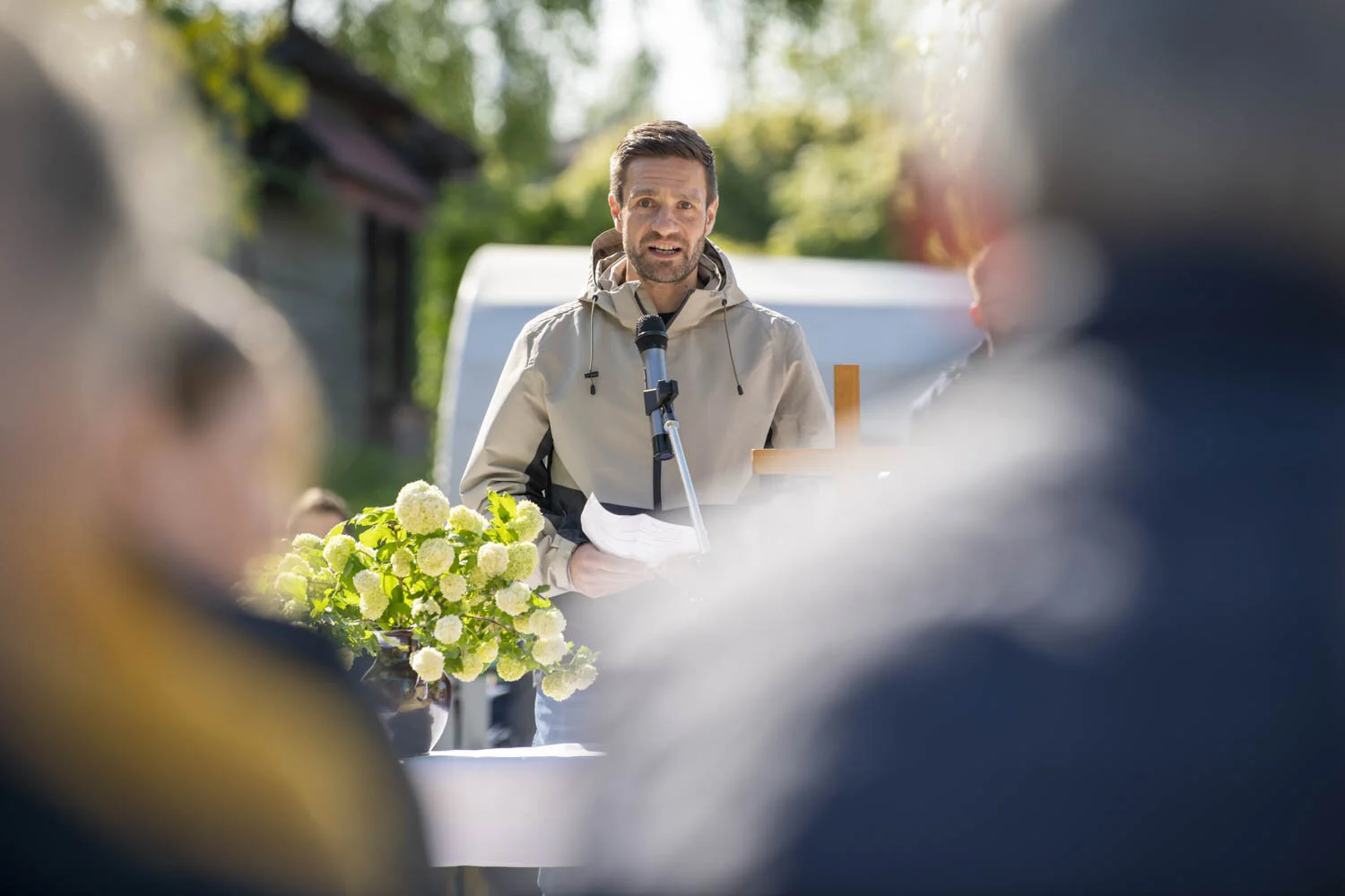 Mann spricht hinter einem Blumengesteck ins Mikrofon