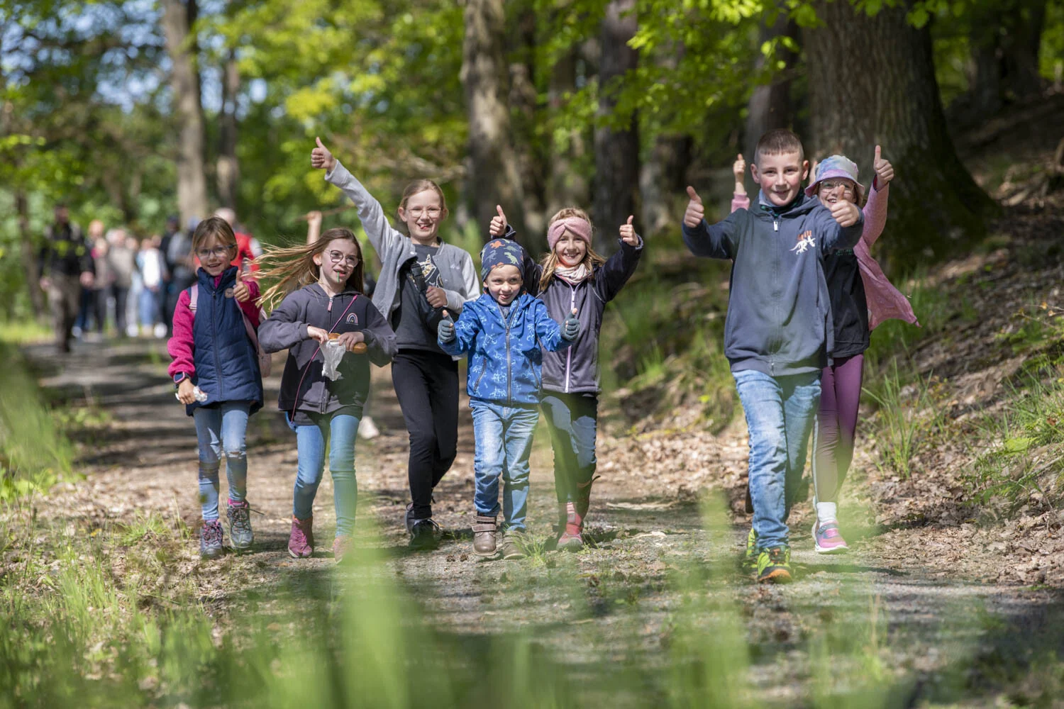 Kinder recken auf einem Waldweg fröhlich die Daumen nach oben