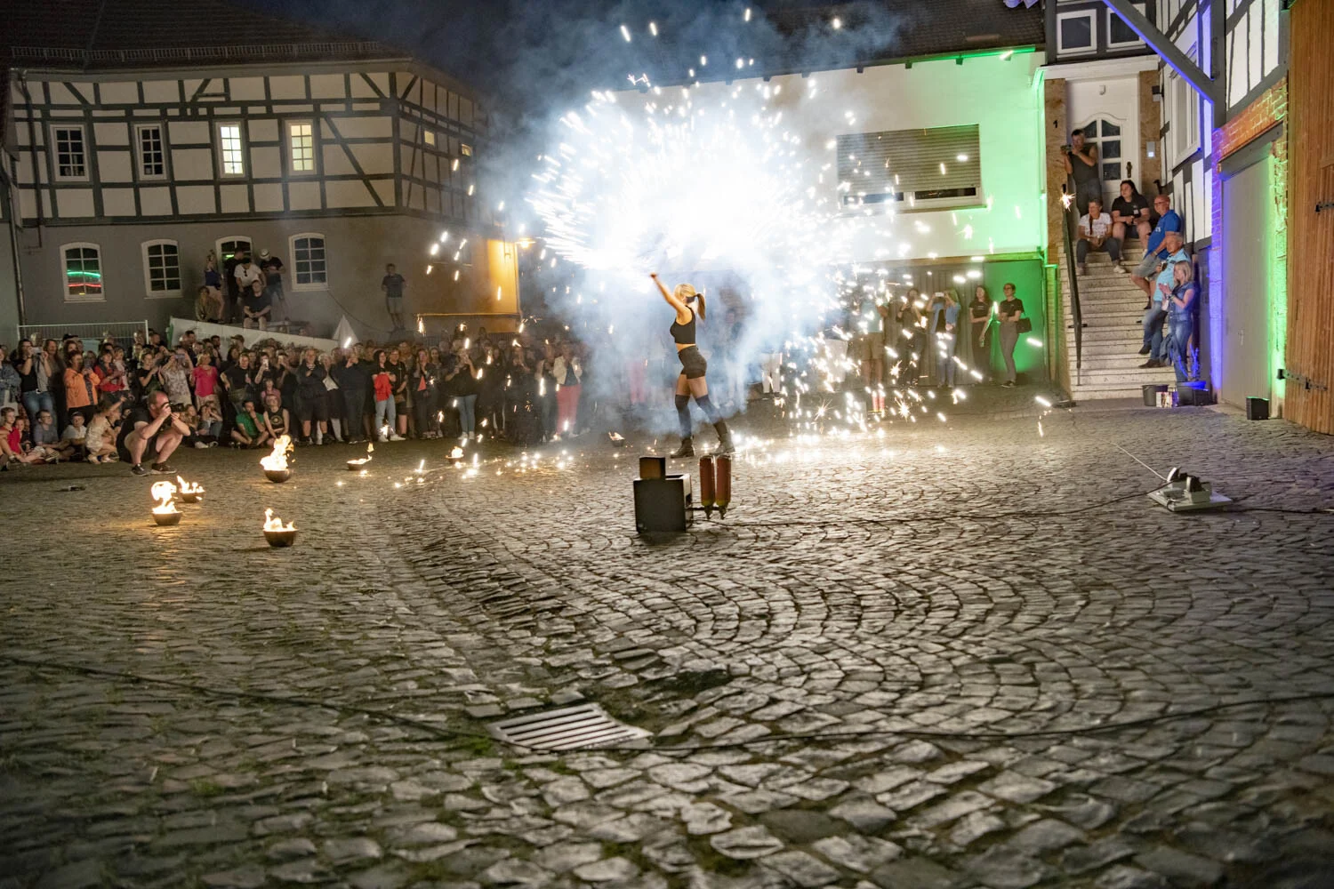 Funkenfontäne auf einem Hof, ringsum zahlreiche Zuschauer