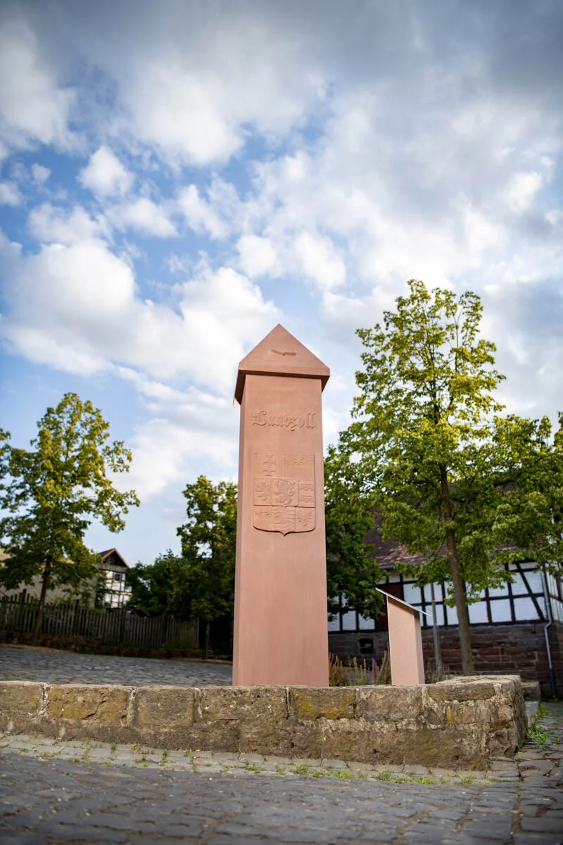 Kleindenkmal mit Pyramidenspitze unter blauem Himmel mit Wolken