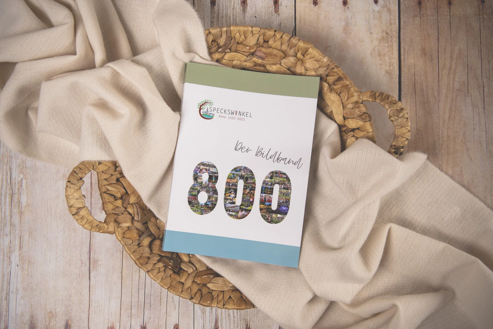 Bildband 800 Jahre Speckswinkel auf einem geflochtenen Korb mit hellem Tuch