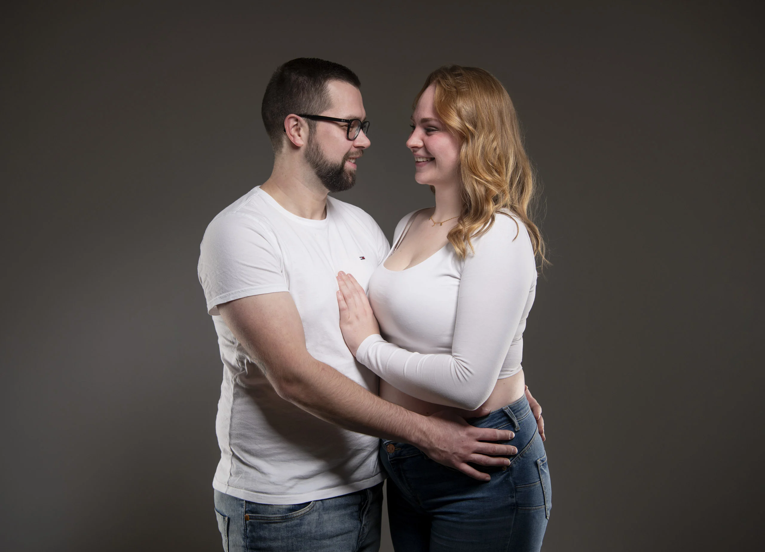 Paarfotos: Paar in weißen Shirts steht eng umschlungen vor einem dunklen Hintergrund