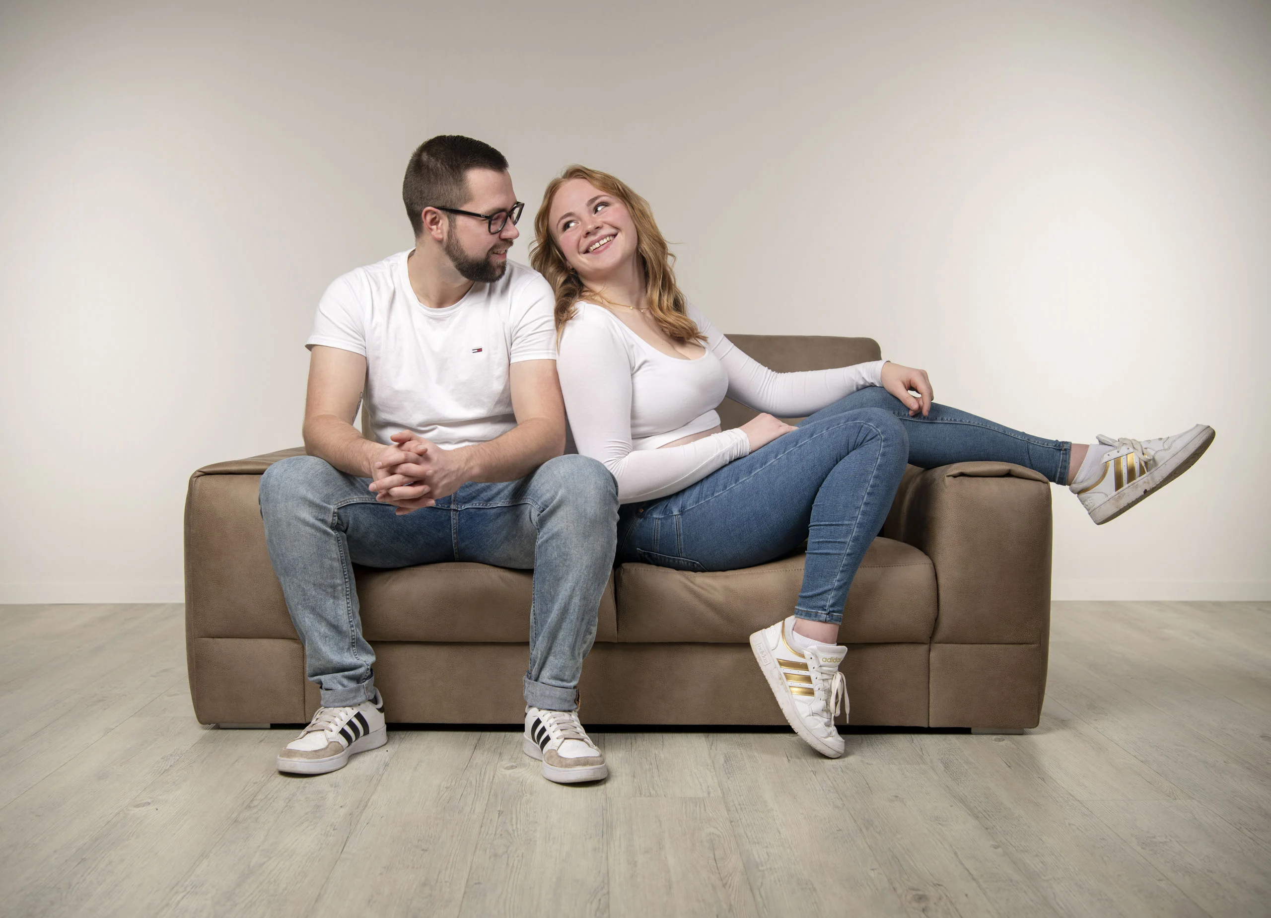 Frau schaut ihren Partner auf dem Sofa lachend an, er lächelt in die Kamera