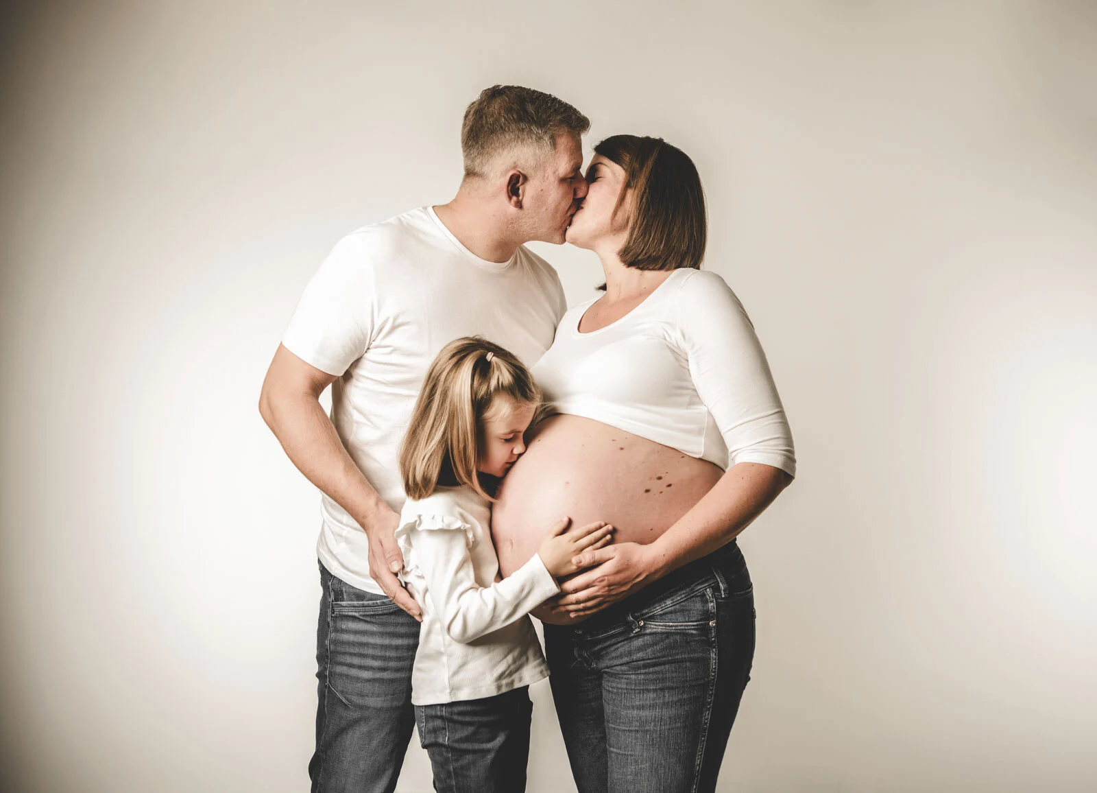 Babybauch-Fotos: Eltern küssen sich, die Tochter gibt dem Babybauch einen Kuss