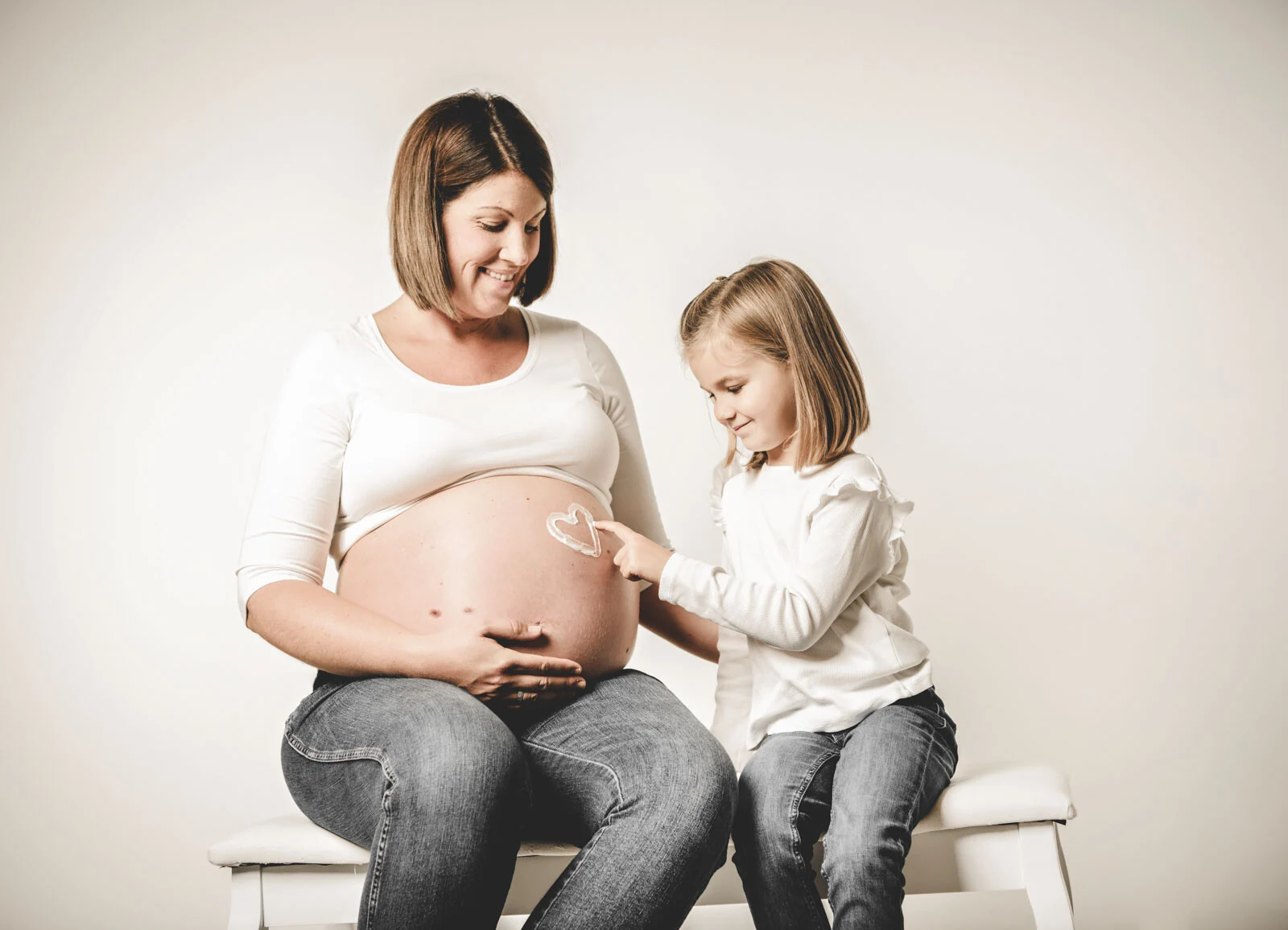 Babybauch-Fotos: Mädchen malt der Mutter ein Herz auf den Babybauch