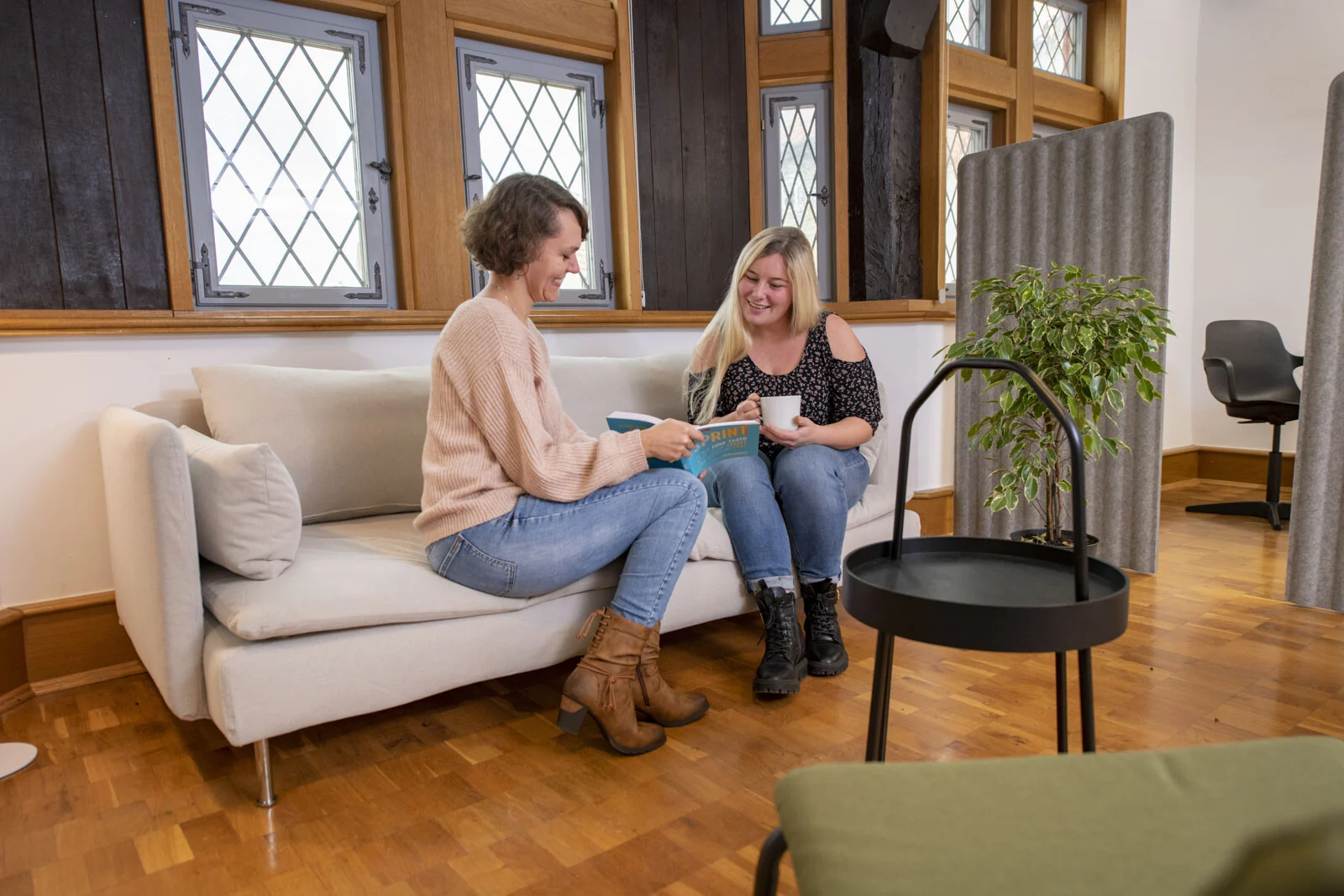 Zwei Frauen sitzen lachend auf einem Sofa vor Bleiglasfenstern
