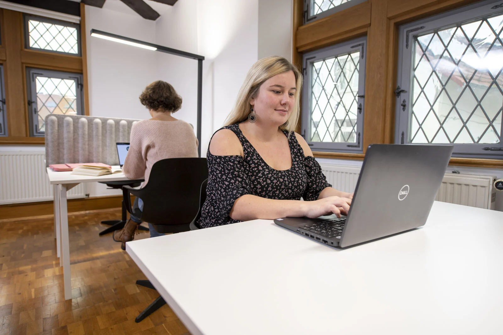 Coworking Space: Frau arbeitet lächelnd am Laptop an einem weißen Schreibtisch