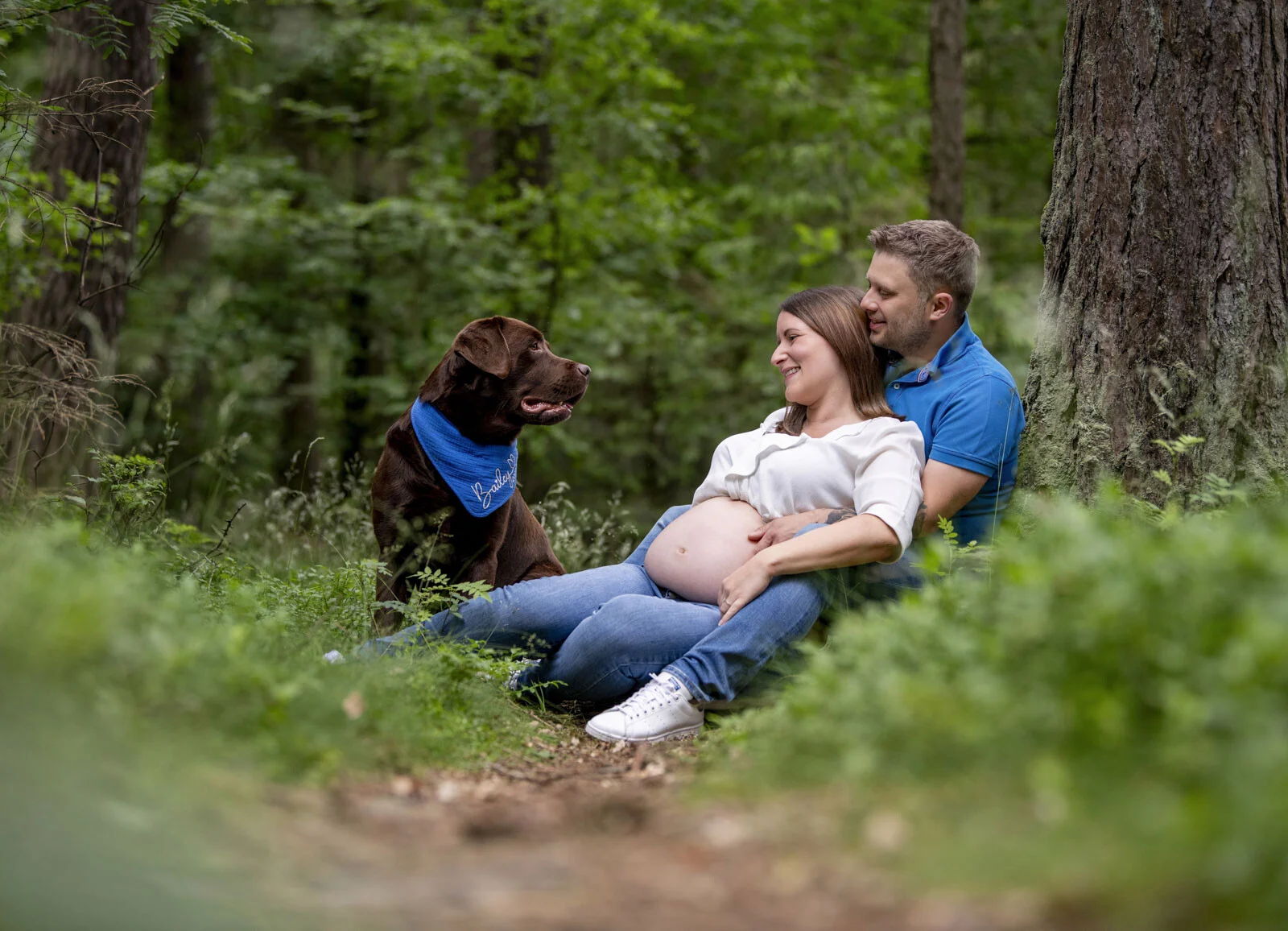 Outdoor-Fotoshooting im Wald: Paar sitzt auf dem Boden, daneben der Labrador mit Halstuch