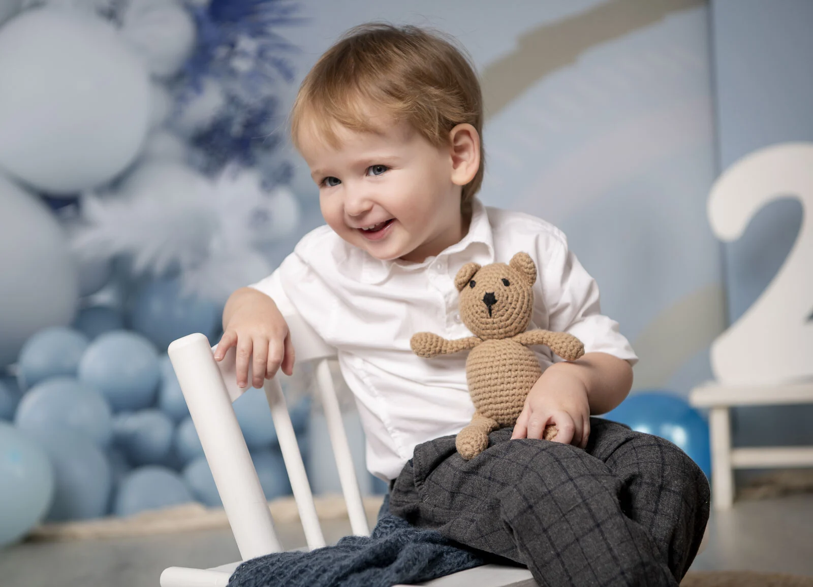 Junge sitzt auf einem Stuhl und hält einen kleinen gehäkelten Teddy im Arm