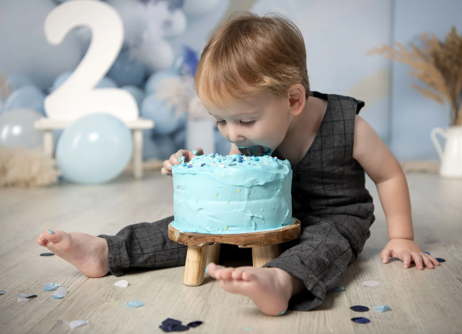 Junge beißt in eine hellblaue Torte auf einem kleinen Holzhocker