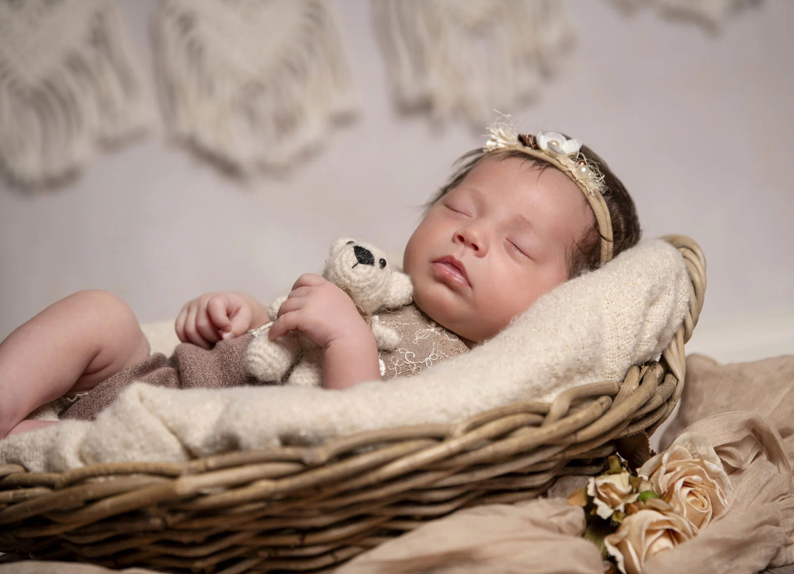 Schlafendes Baby hält einen kleinen Teddy im Arm, eingekuschelt im Weidenkorb