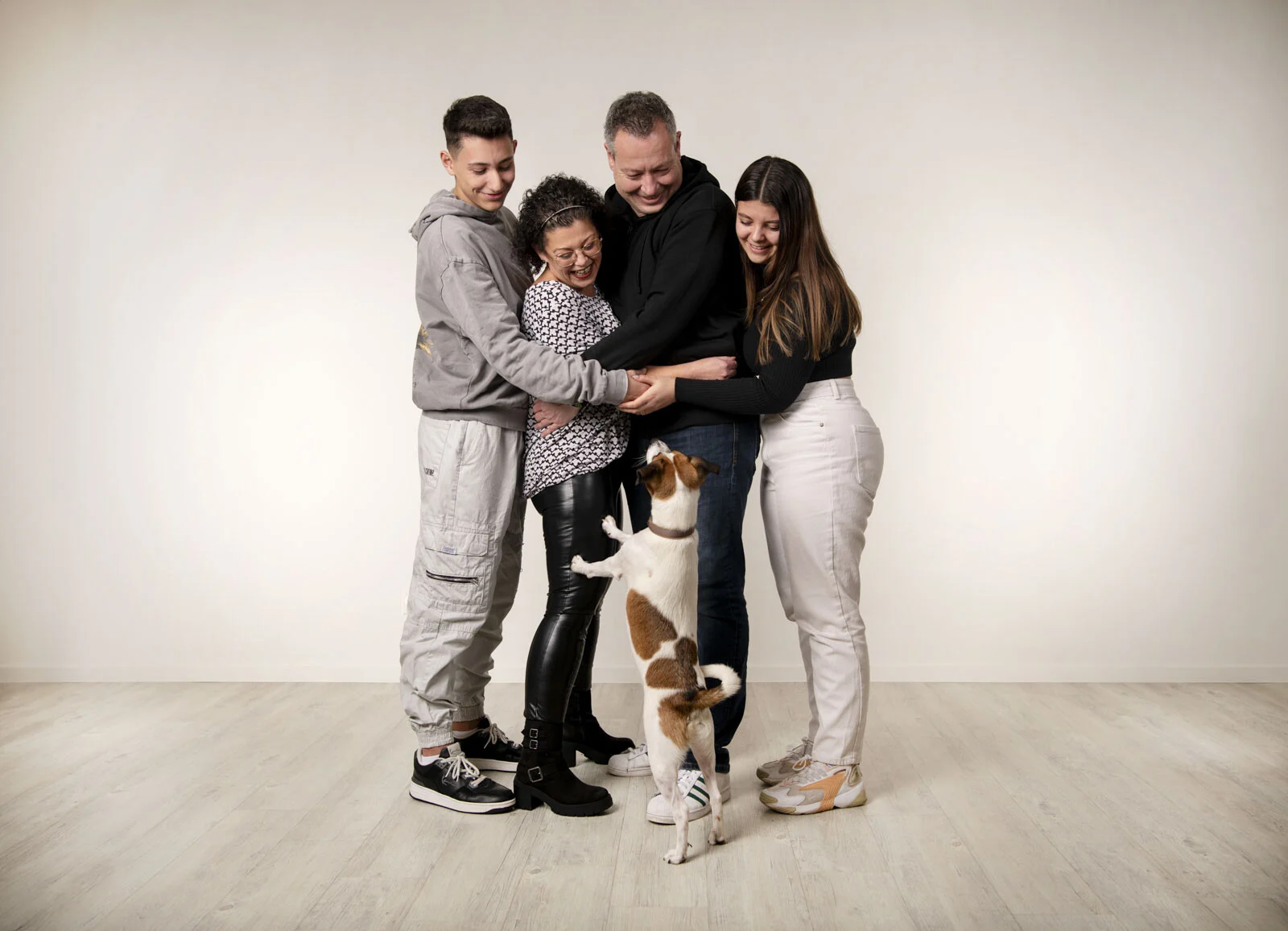 Familie umarmt sich, der kleine Hund springt an den Beinen hoch