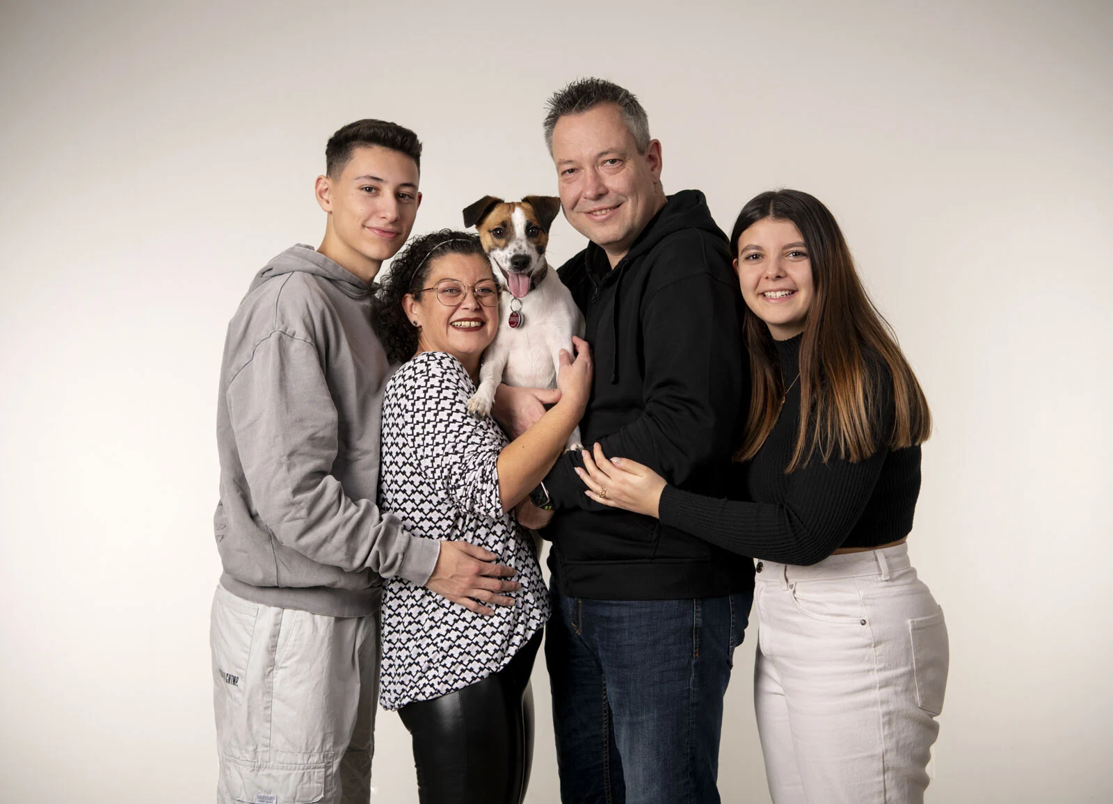 Familie steht eng zusammen, die Mutter hält den kleinen Hund auf dem Arm