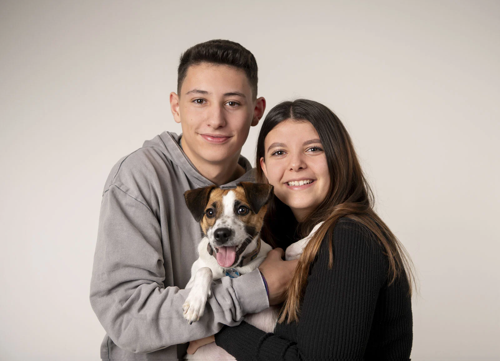 Bruder und Schwester halten lächelnd den kleinen Familienhund im Arm