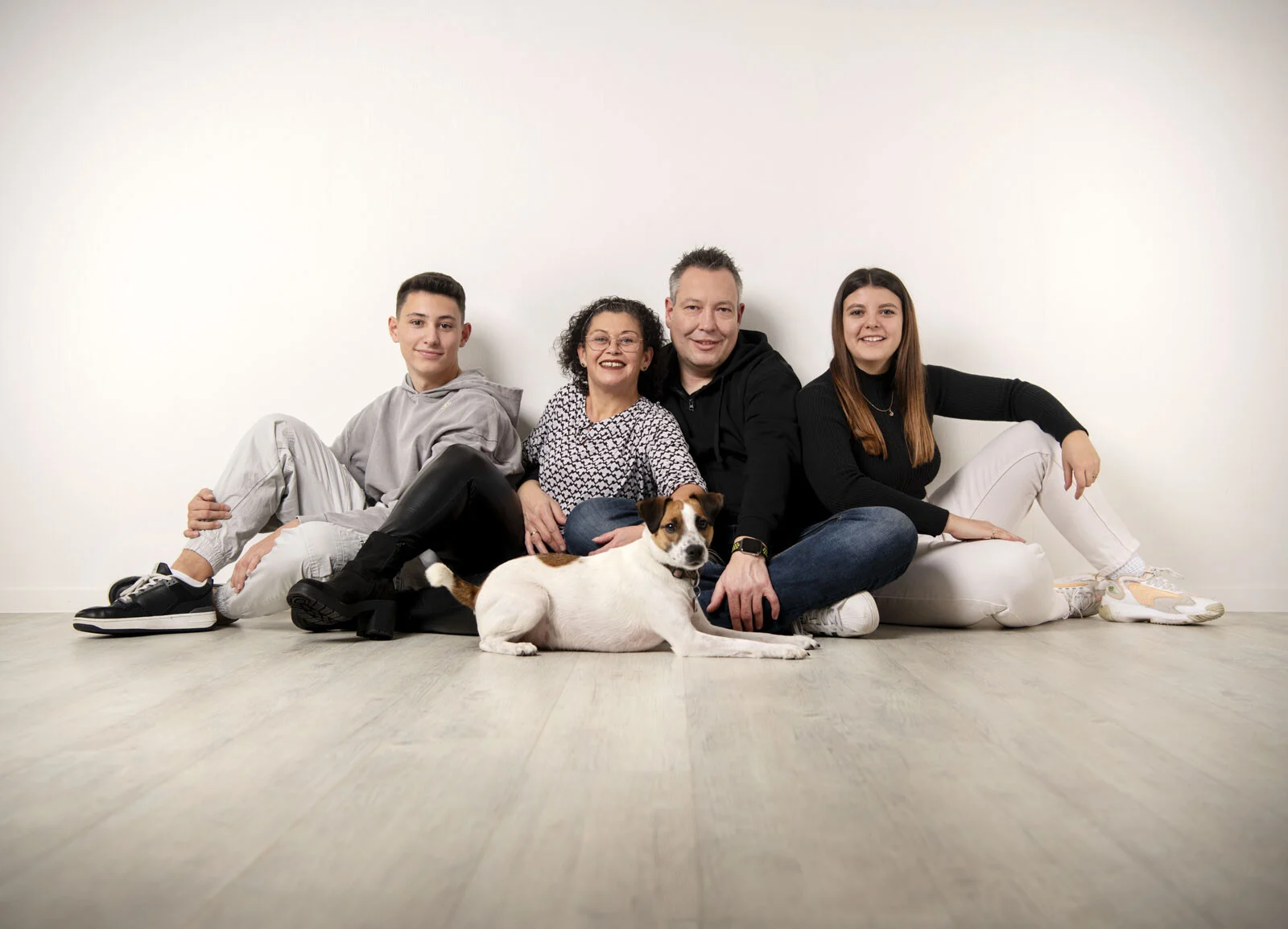 Familienfoto als Weihnachtsgeschenk: Familie sitzt mit Hund entspannt auf dem Boden