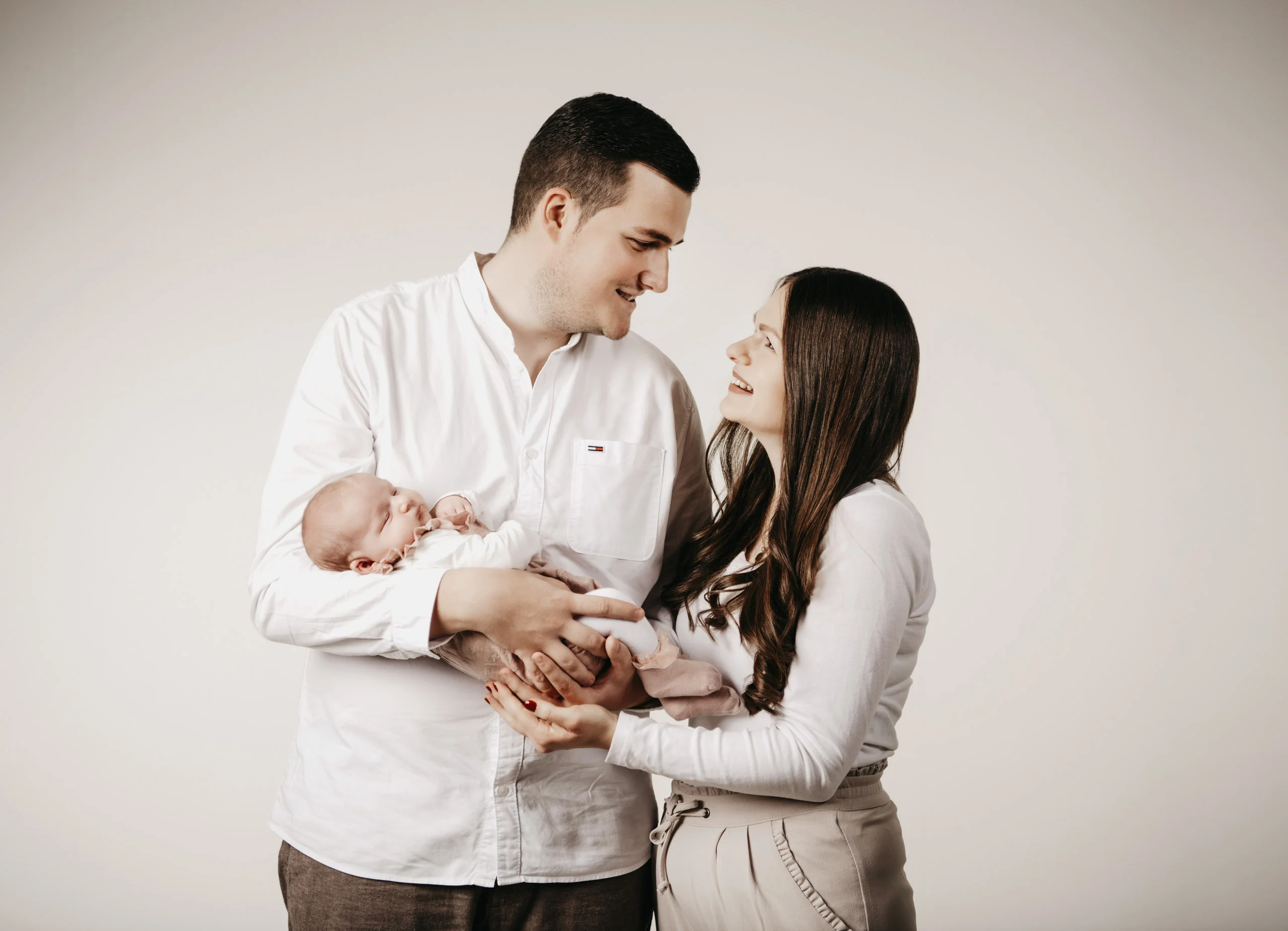 Eltern schauen sich verliebt an, der Vater hält das Baby im Arm
