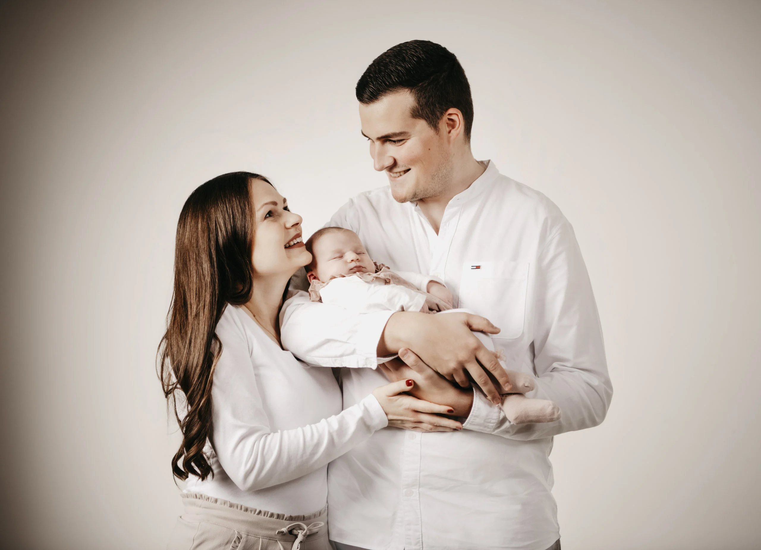 Junges Paar hält das Baby zwischen sich, die Mutter schaut zum Vater hoch