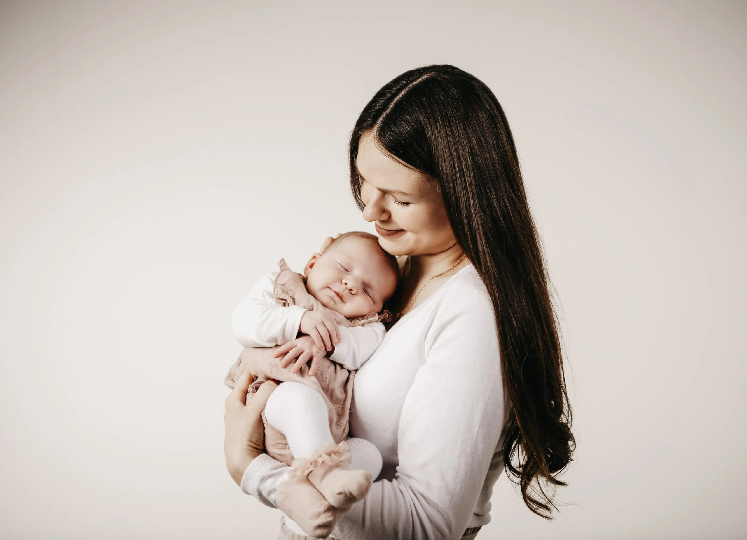 Familienfotos mit Baby: Mutter mit langen Haaren kuschelt mit ihrem schlafenden Baby