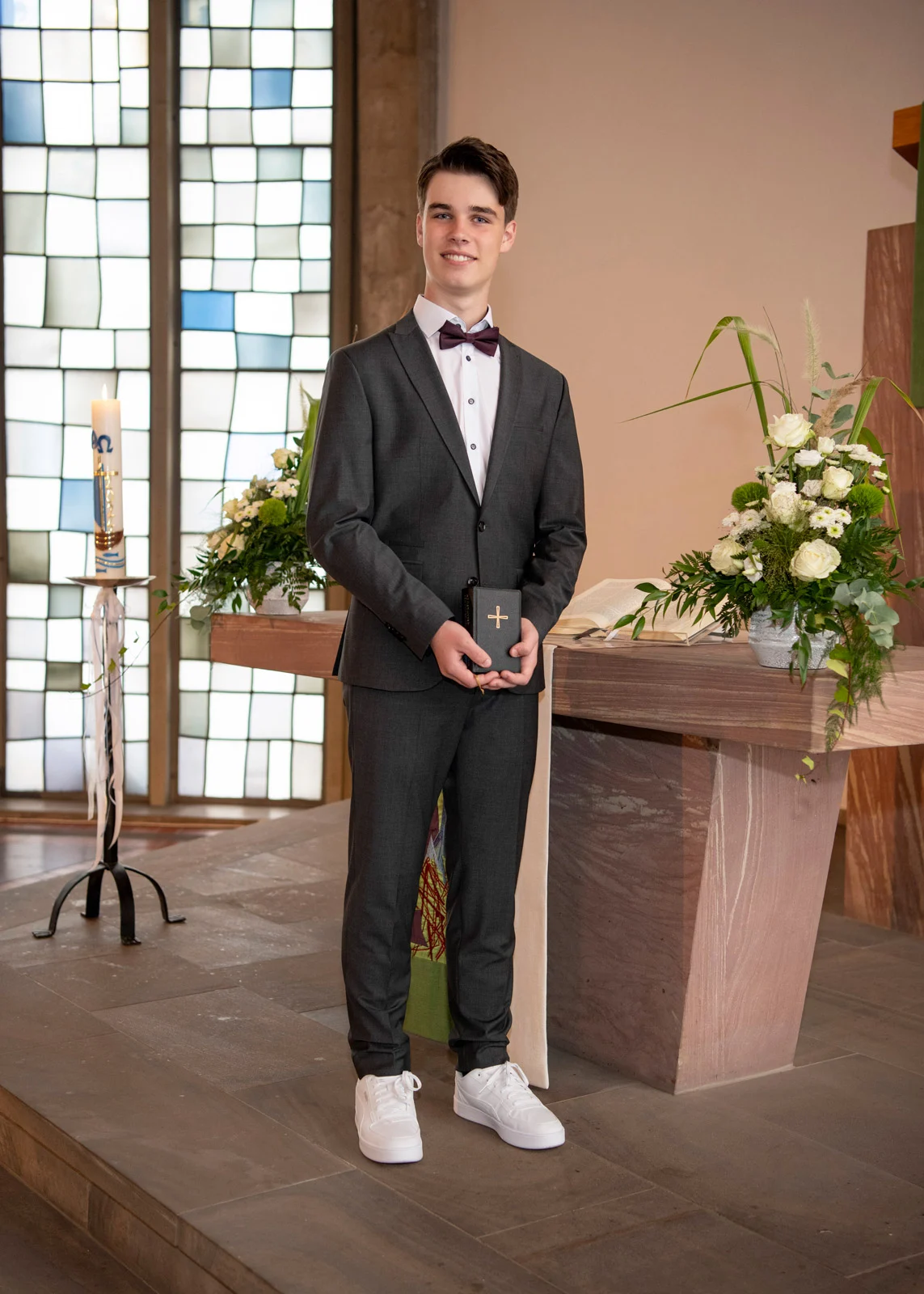 konfirmation kommunion taufe | Peter Lauritis Photography Konfirmand im dunklen Anzug steht vor dem Altar in der Kirche