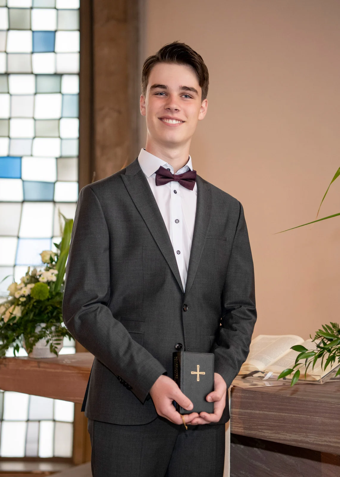 konfirmation kommunion taufe | Peter Lauritis Photography Konfirmand im grauen Anzug mit Fliege hält sein Gesangbuch